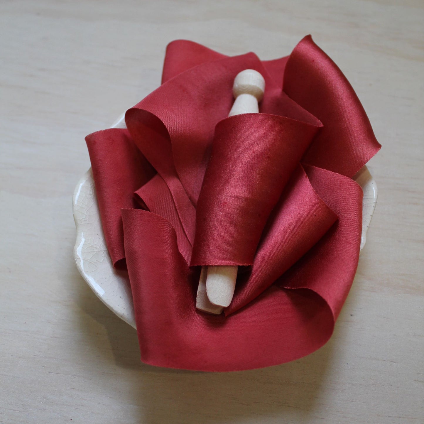 Christmas red silk charmeuse ribbon coiled neatly, emphasizing its seamless, handcrafted quality.