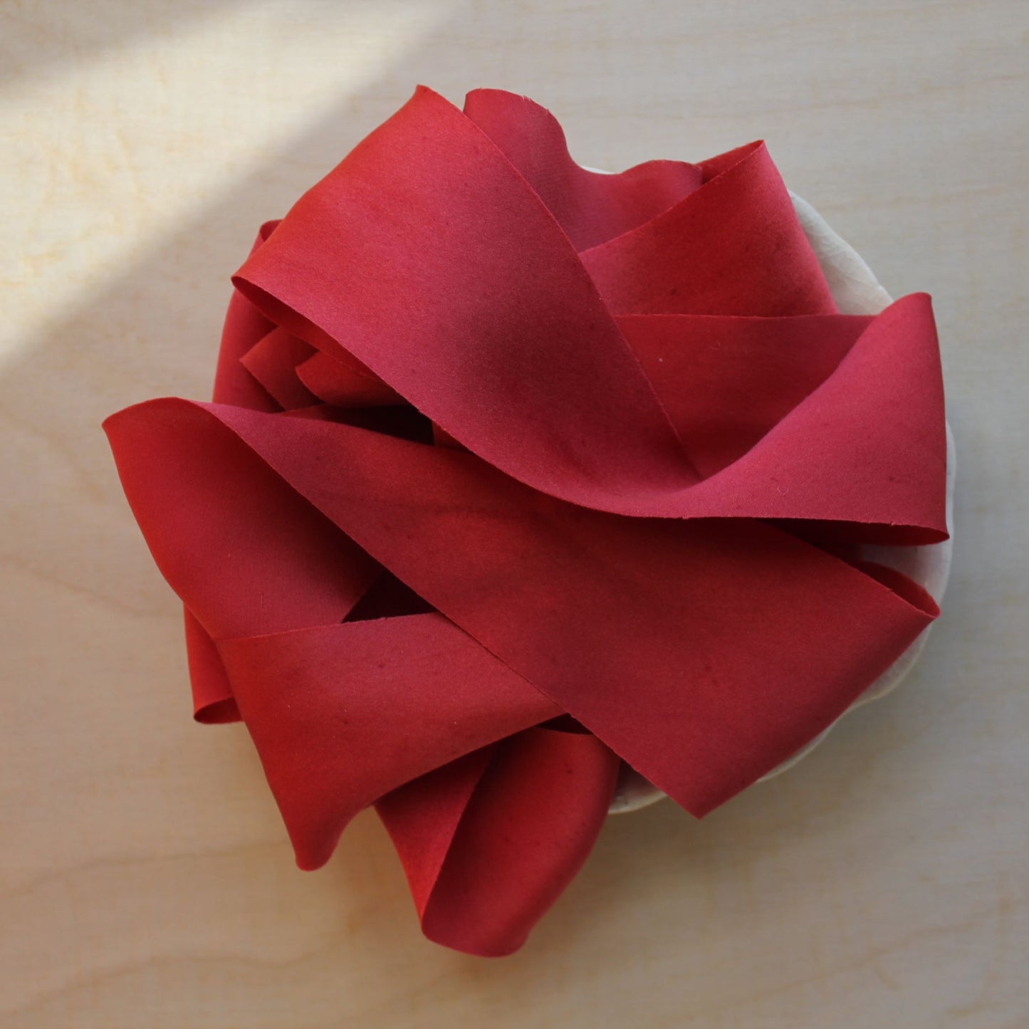 Christmas red silk charmeuse ribbon, hand-cut on the bias, elegantly draped to showcase its soft sheen and fluidity.