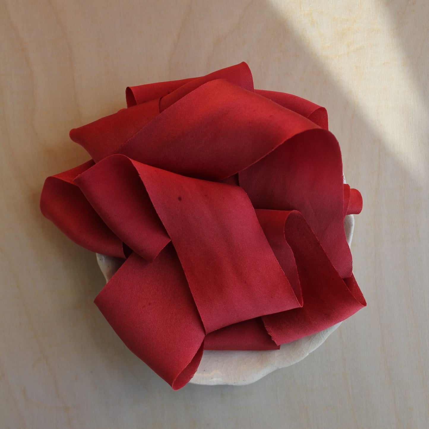 Soft silk ribbon in Christmas red displayed on a wood spool, highlighting the ribbon's subtle shine.