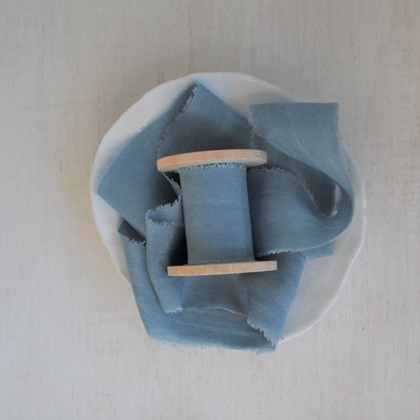 Blue silk crepe de chine hand-torn ribbon on wooden spool.