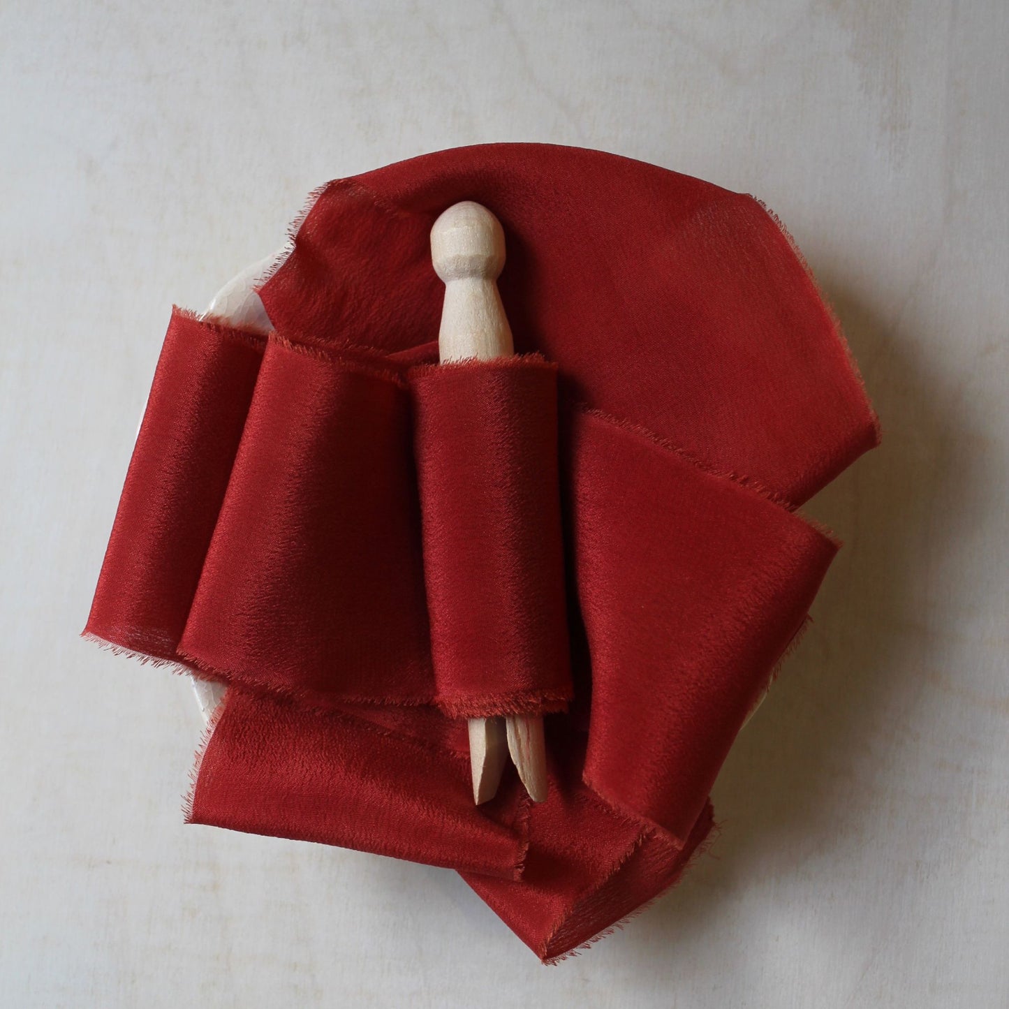 Hand-torn Christmas red silk crepe de chine ribbon draped over a wooden surface.