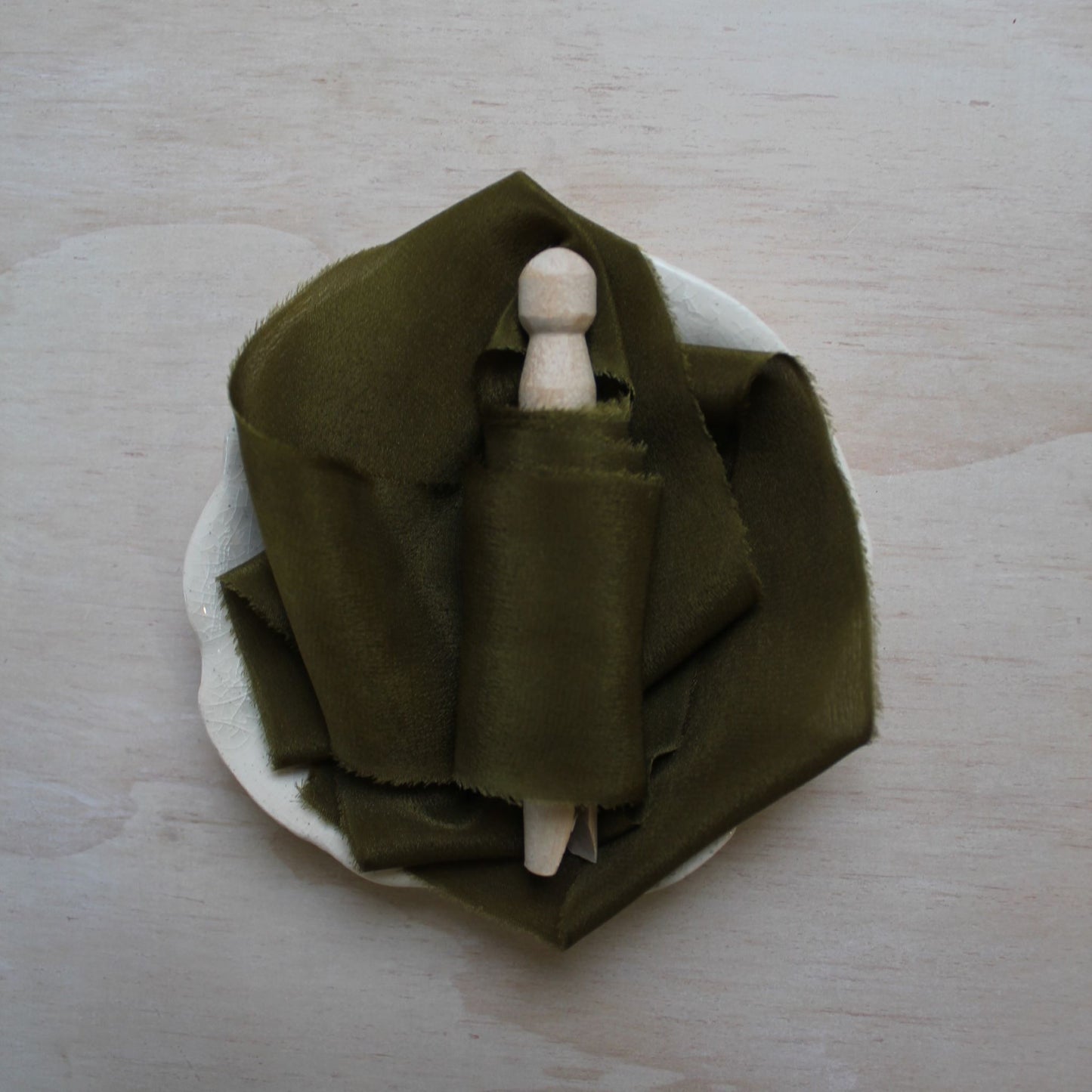 Hand-dyed moss green silk ribbon coiled neatly on a wooden spool