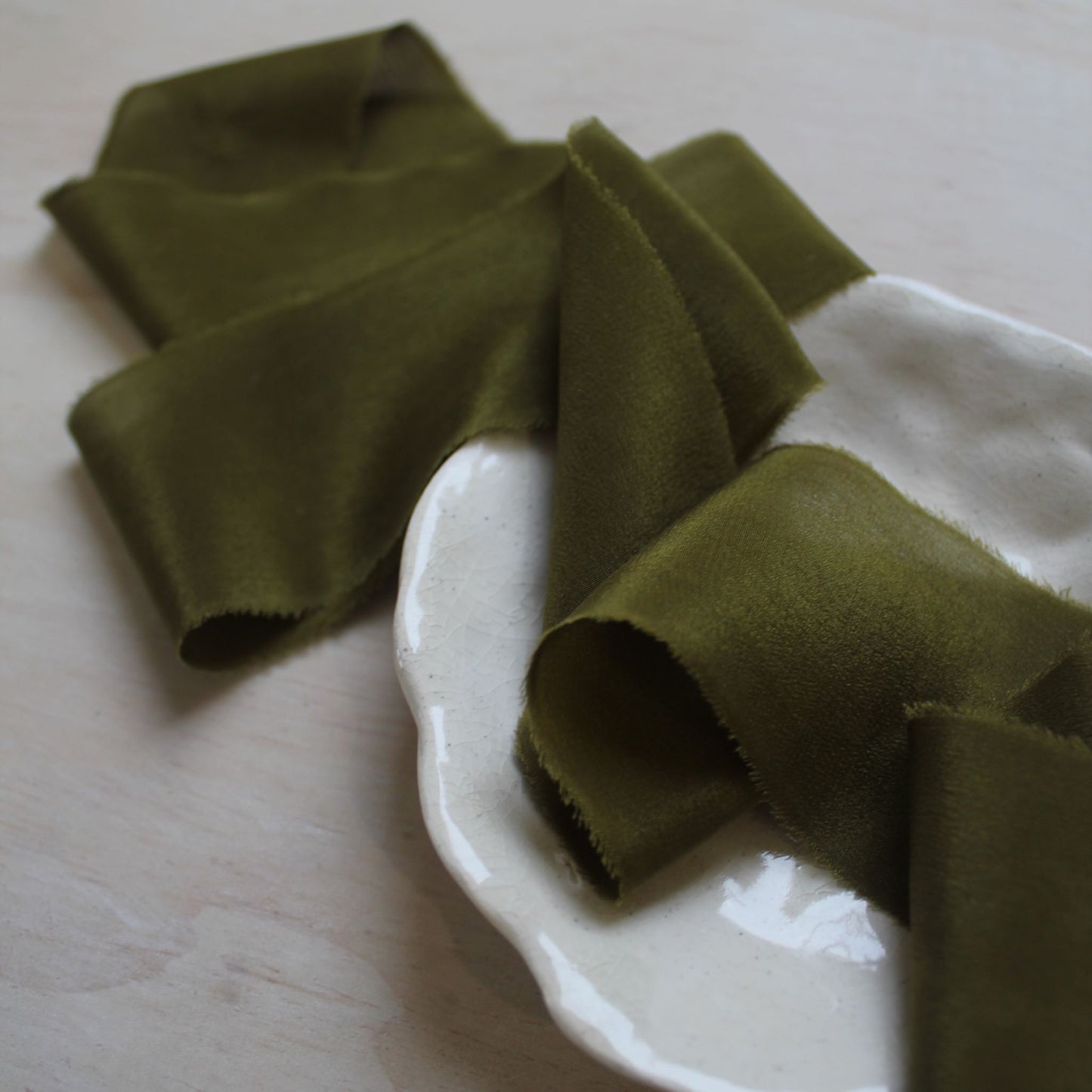 Close-up of moss green silk ribbon showcasing its soft, feathered edges.
