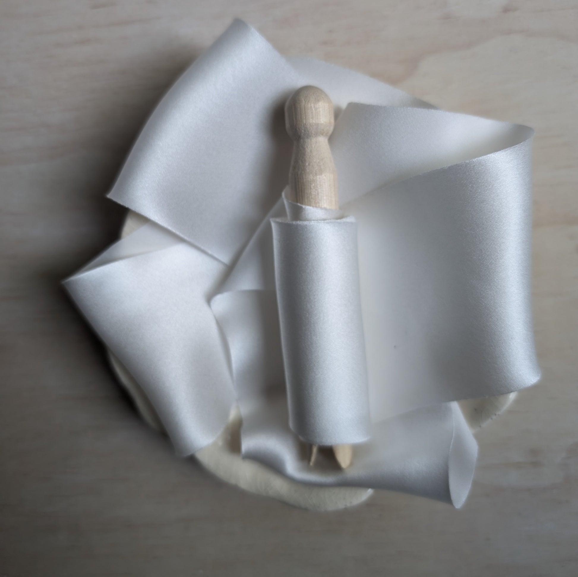 White silk charmeuse ribbon hand-cut on the bias, elegantly draped to highlight its sheen and fluidity.