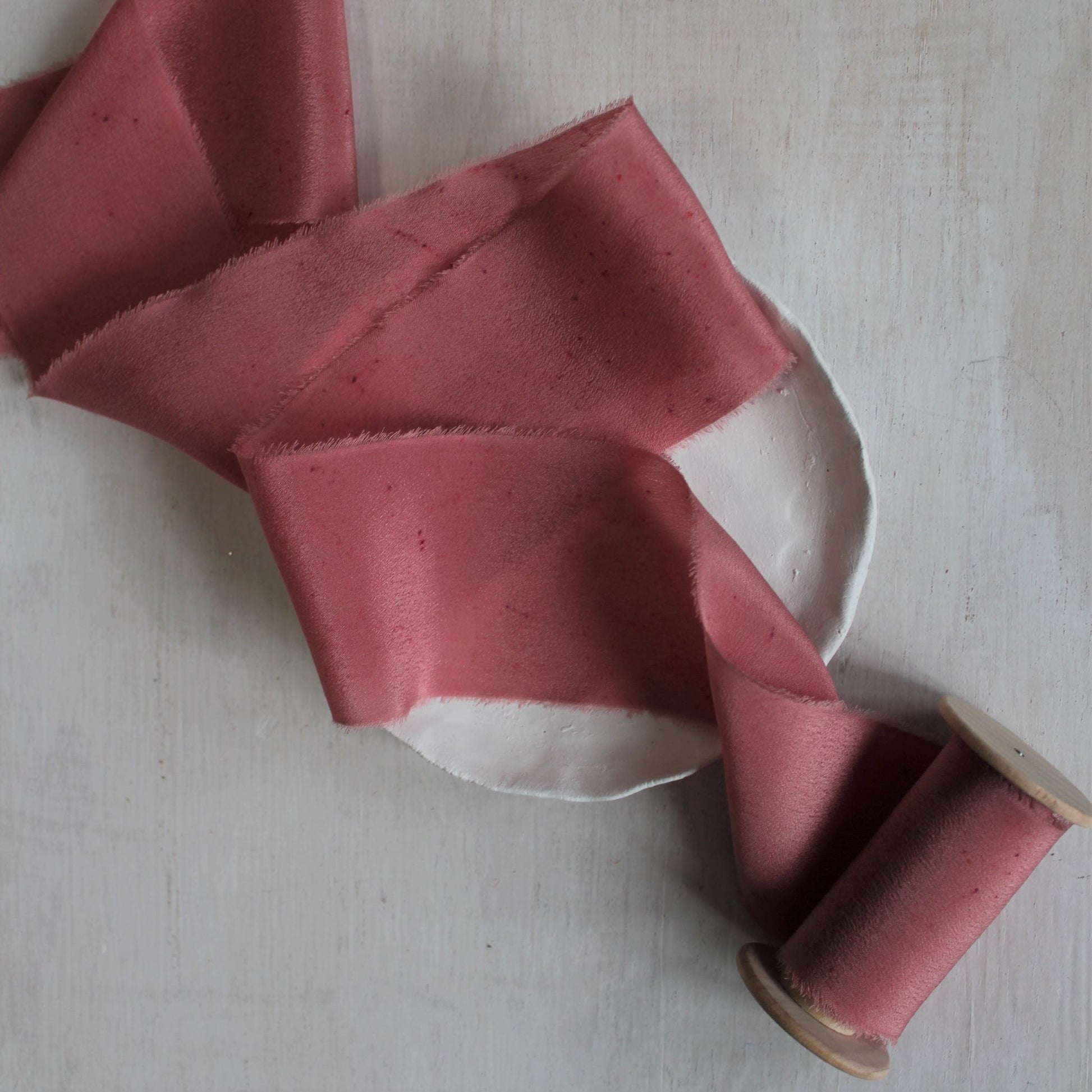 Soft, hand-torn berry silk crepe de chine ribbon with delicate feathered edges on a wooden spool.