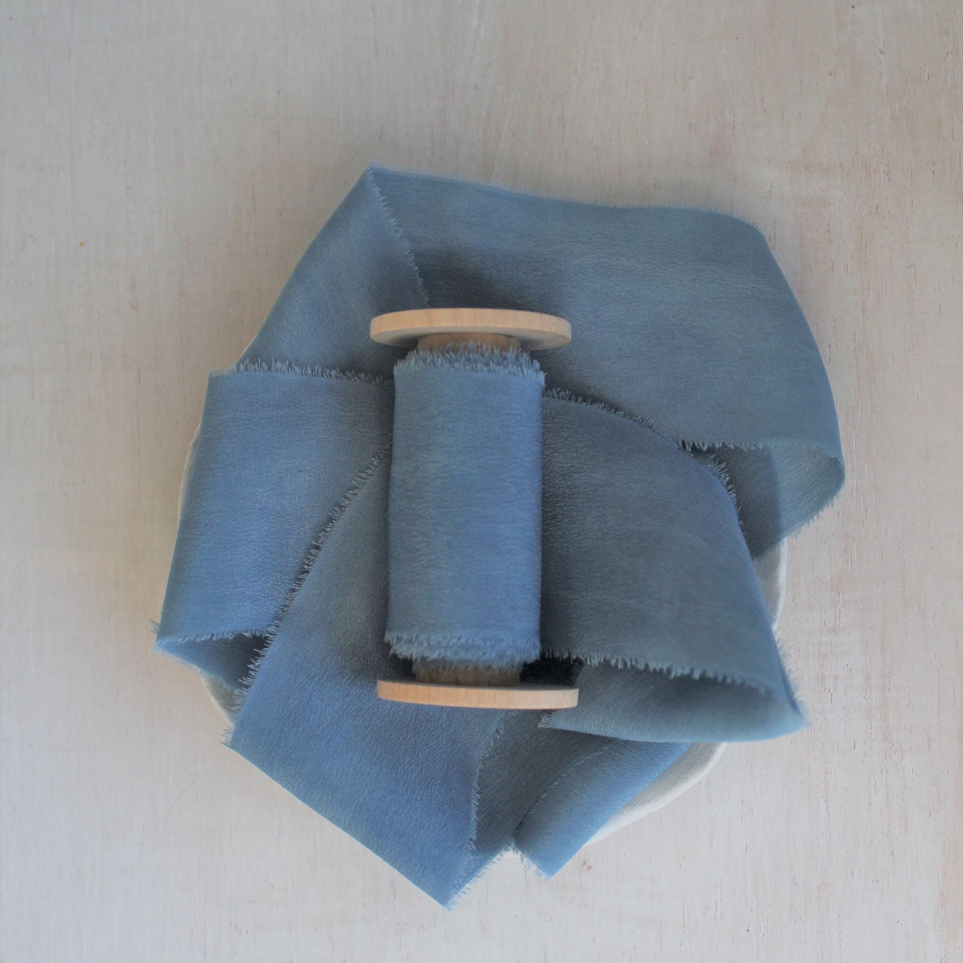Blue silk crepe de chine hand-torn ribbon on wooden spool.