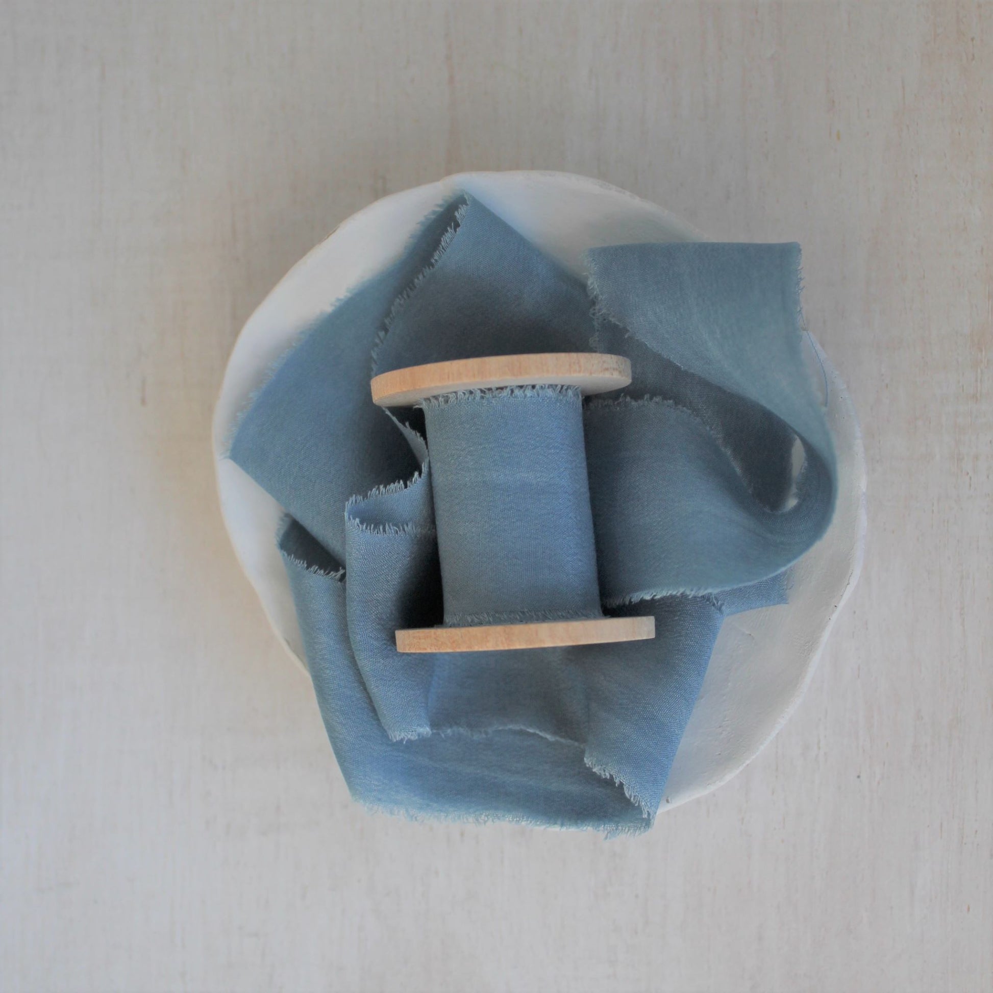 Blue silk crepe de chine hand-torn ribbon on wooden spool.
