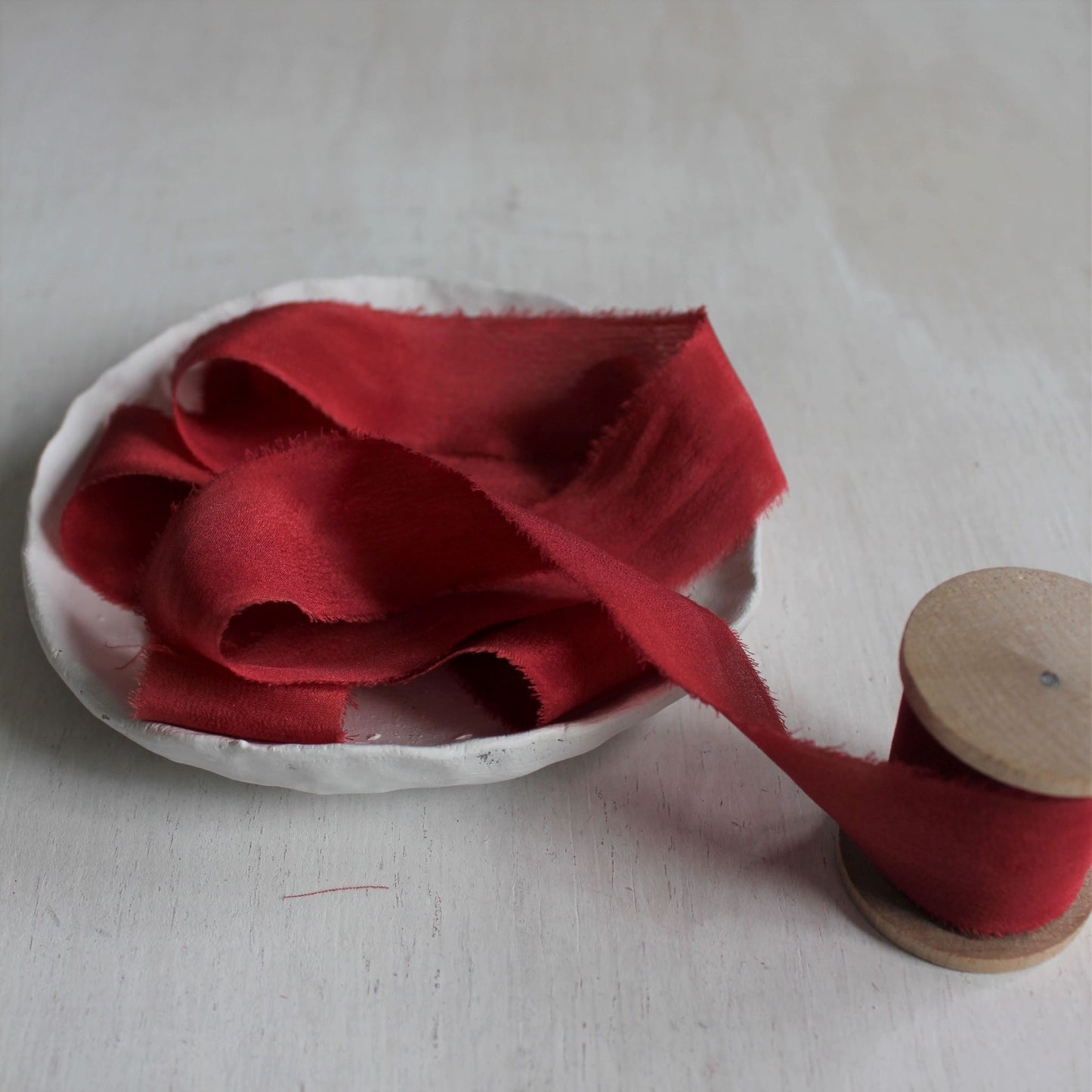 Hand-dyed Christmas red silk ribbon coiled on a wooden spool.