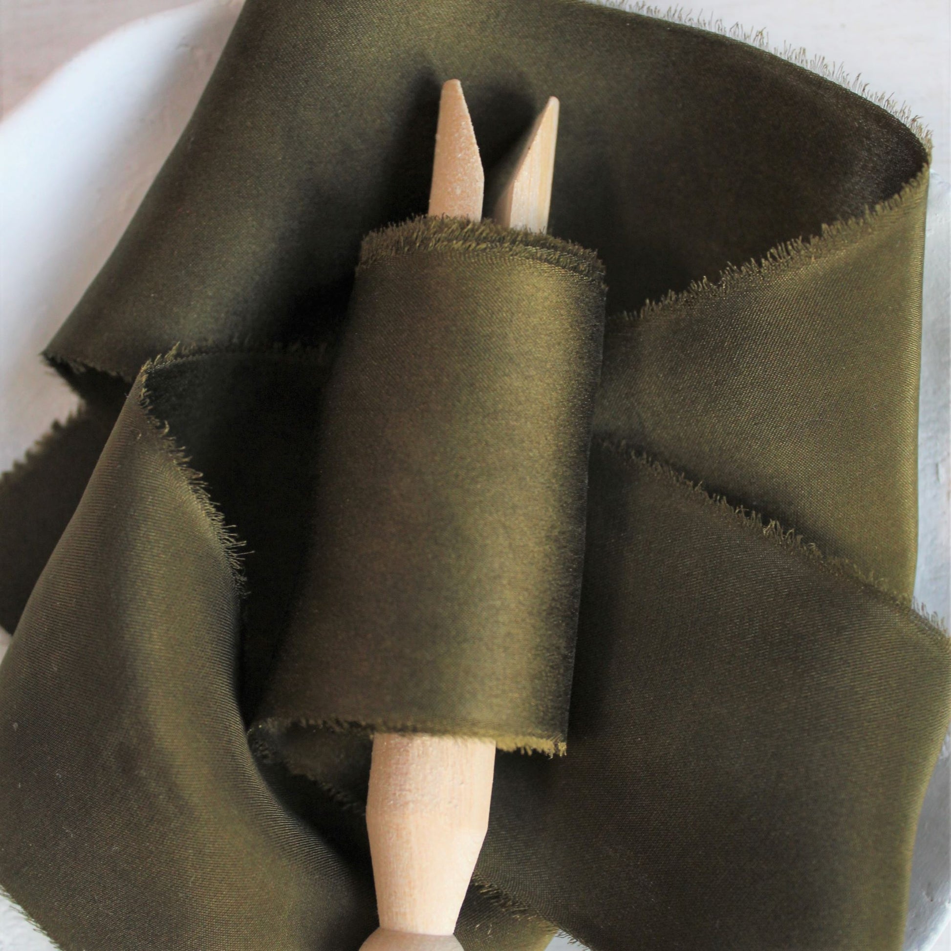 Close-up of hand-torn dark moss silk charmeuse ribbon showcasing feathered edges