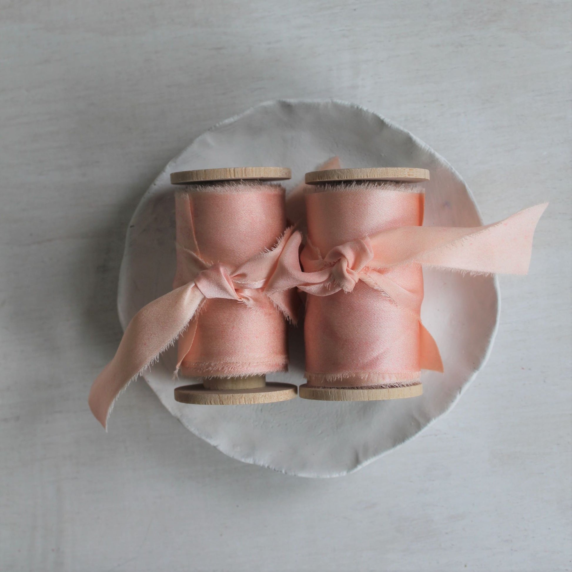two pink blush silk charmeuse hand-torn ribbons on wood spools