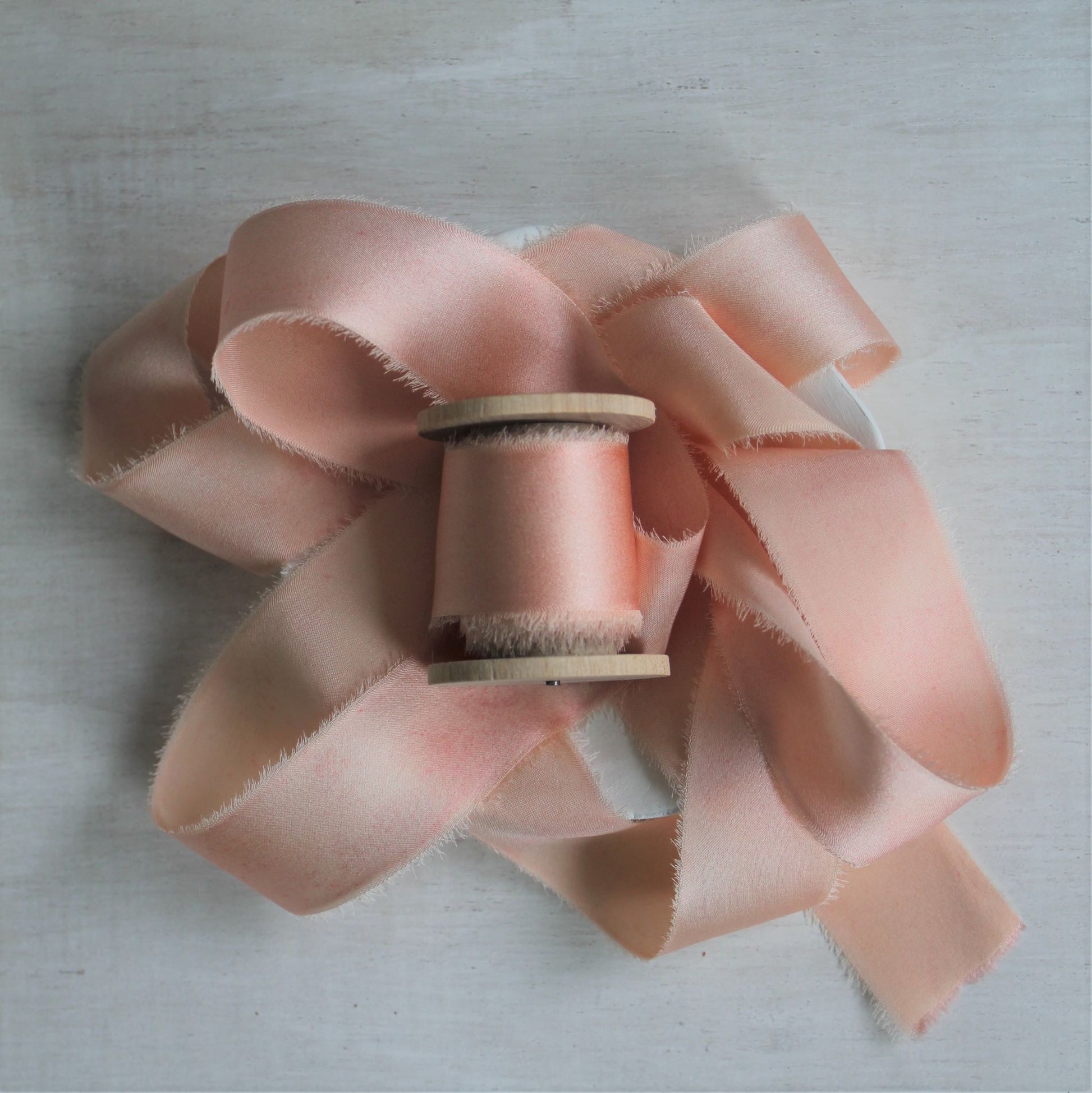 Pink blush silk charmeuse hand-torn ribbon on wooden spool.