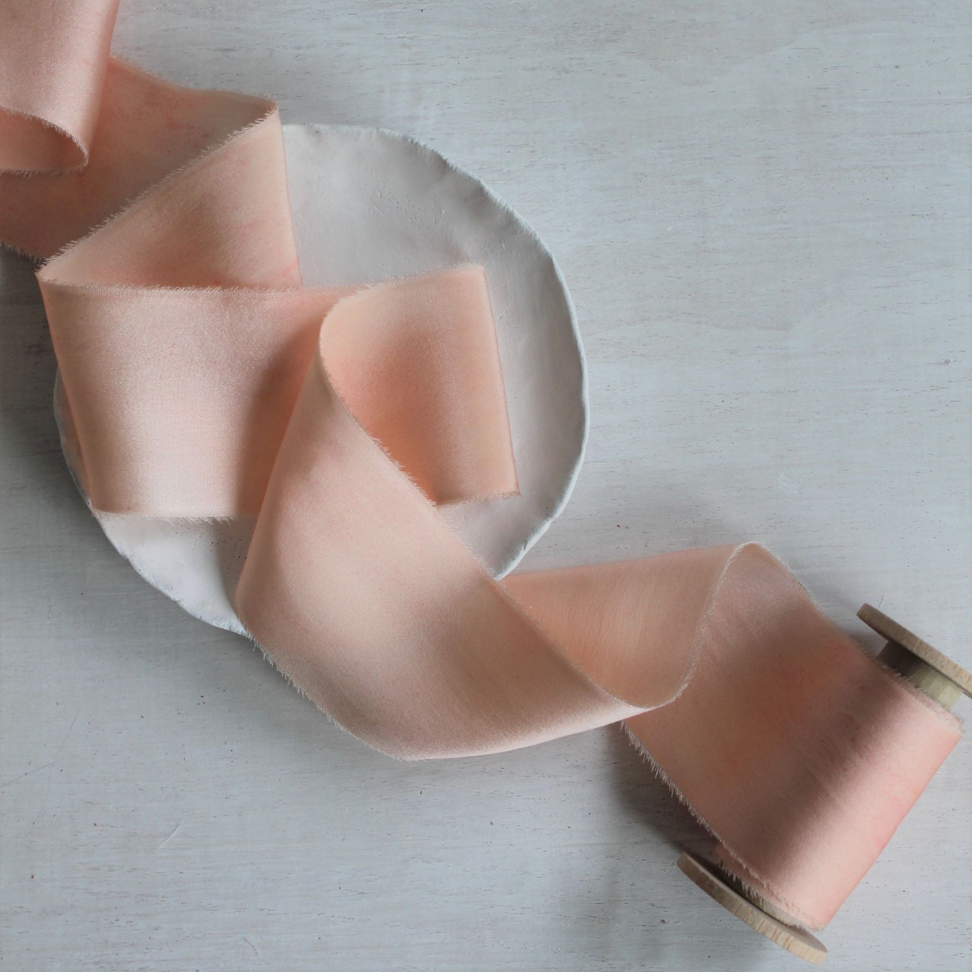Close-up of hand-torn pink blush silk charmeuse ribbon showcasing feathered edges.
